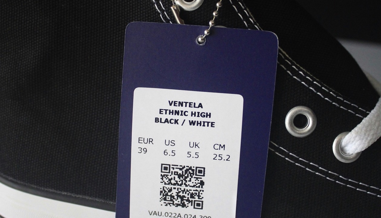 A swing tag on a canvas shoe, printed with a size grid and a QR code.