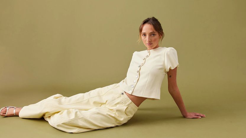 A model seated on a studio floor in a cream linen outfit.