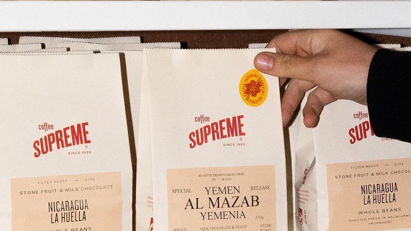 A hand placing a sticker on a bag of coffee on a shelf.