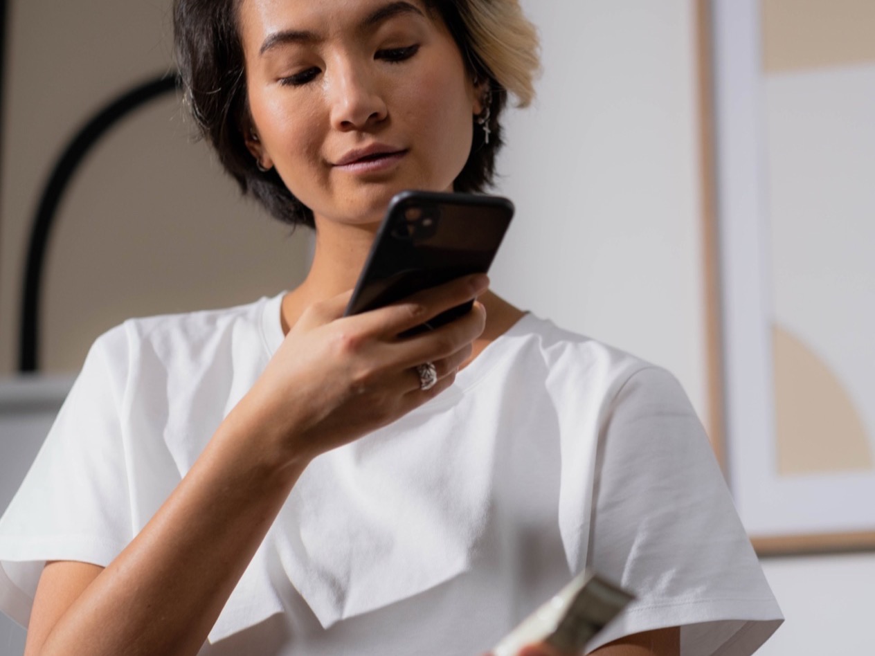 A person holds a product tube and reads its page on a phone.