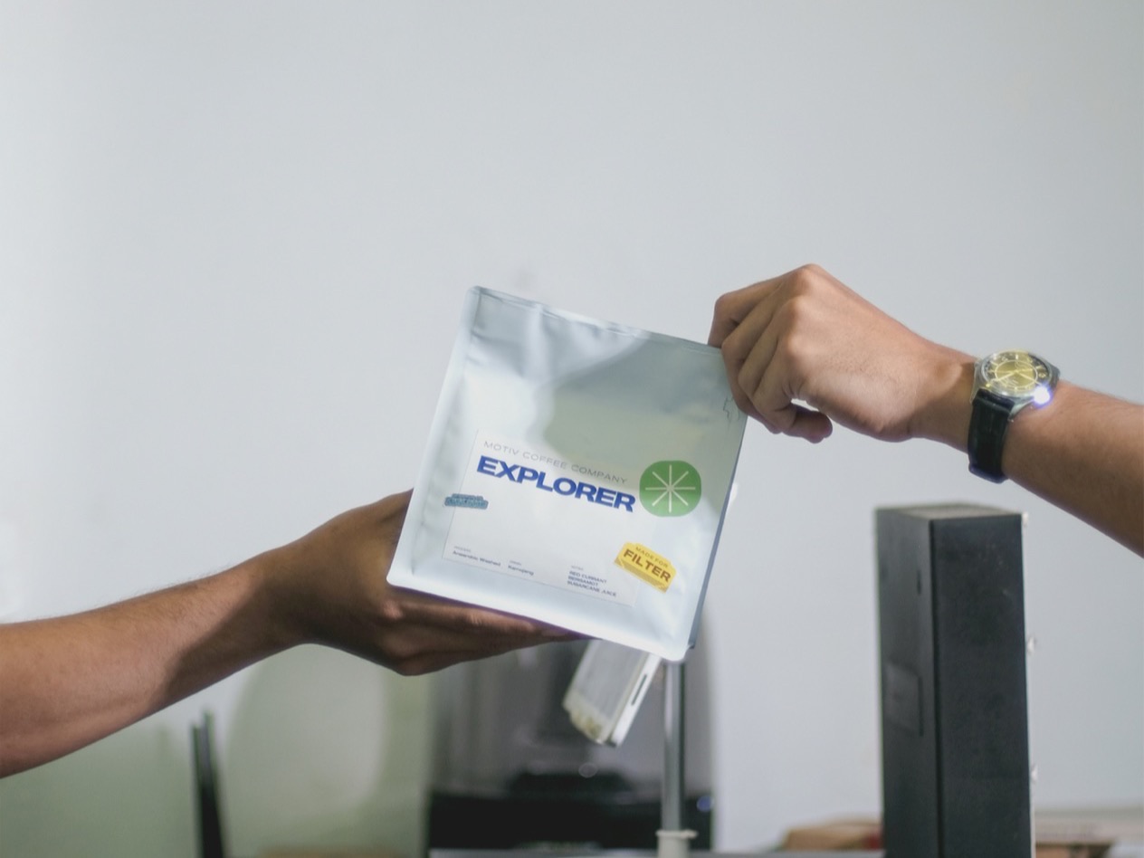 Two people pass a foil coffee bag across a counter.