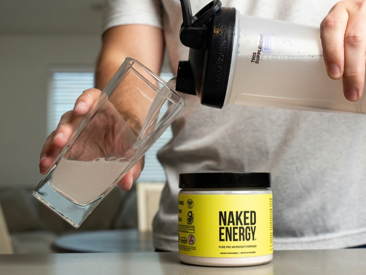 A person pours a mixed supplement drink into a glass beside its labelled tub.