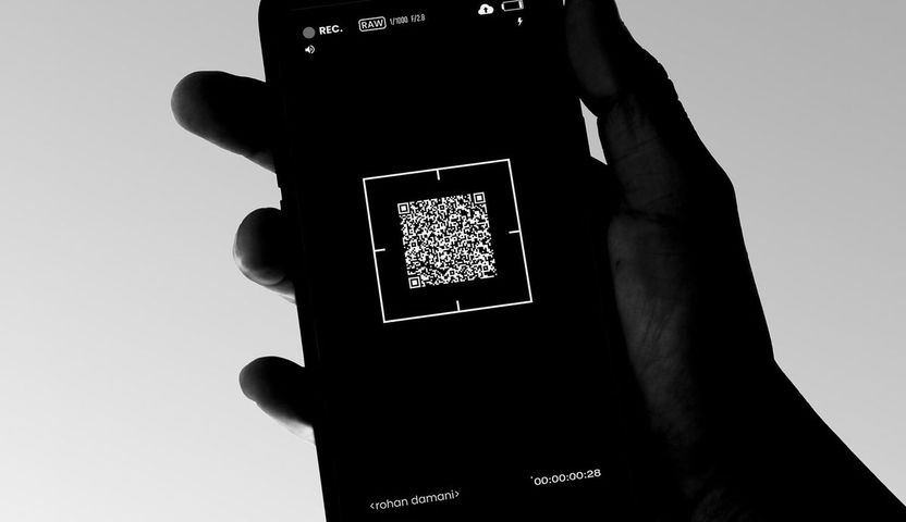 A gloved hand holding a phone that is scanning a small square code.